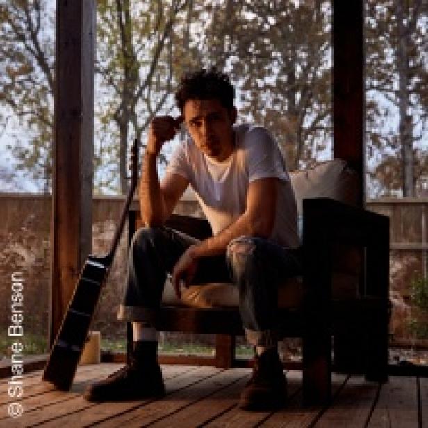 Ein Mann sitzt mit einer Gitarre auf einer Veranda.