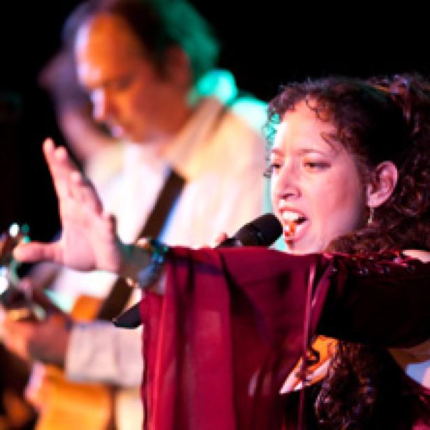 Eine Sängerin tritt mit einem Mikrofon vor einem Gitarristen auf.