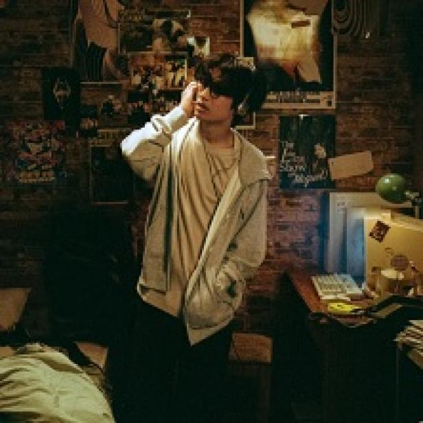 Ein junger Mann mit Brille steht in einem Zimmer mit vielen Postern an der Wand.