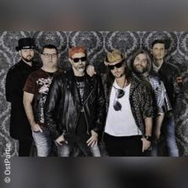 Eine Band posiert vor einer gemusterten Wand für ein Gruppenfoto.