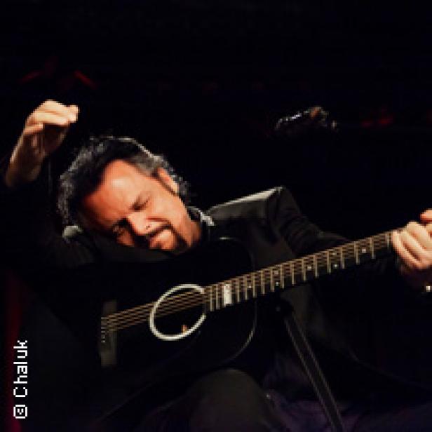 Ein Mann mit Gitarre auf einer Bühne im dunklen Licht.