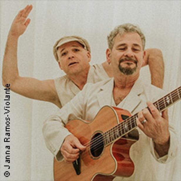 Zwei Männer posieren, einer spielt Gitarre, der andere hebt die Hand.