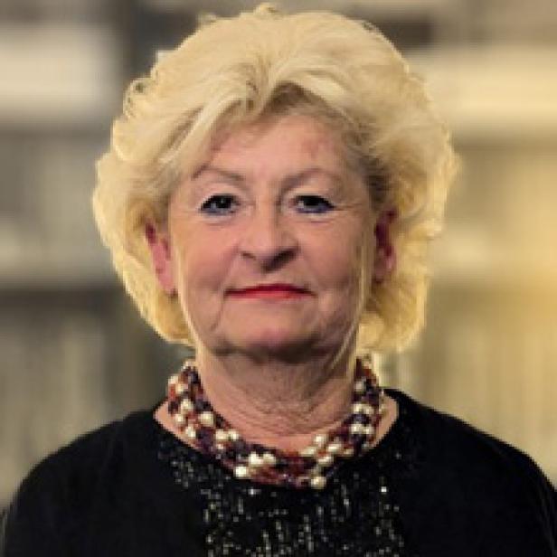 Porträt einer älteren Frau mit blonden, lockigen Haaren und einer Perlenkette.