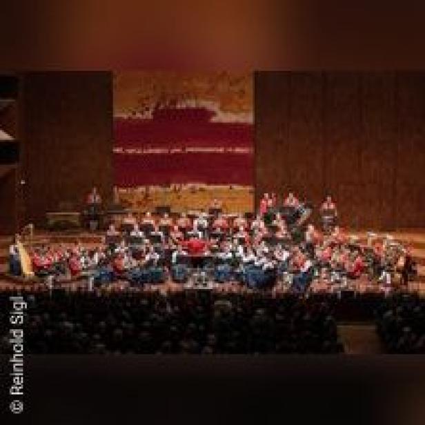Ein großes Orchester spielt auf einer Bühne vor einem Publikum.