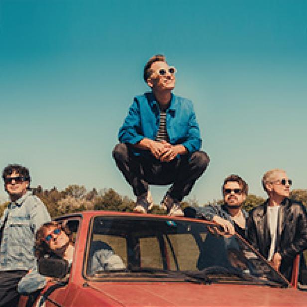 Die Band Giant Rooks posiert auf und an einem roten Auto vor blauem Himmel.