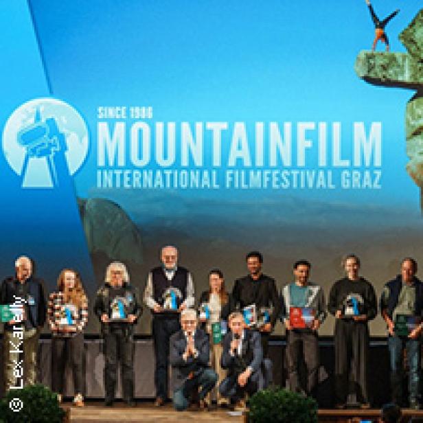 Eine Gruppe von Menschen steht auf einer Bühne vor dem Mountainfilm International Filmfestival Graz Logo.