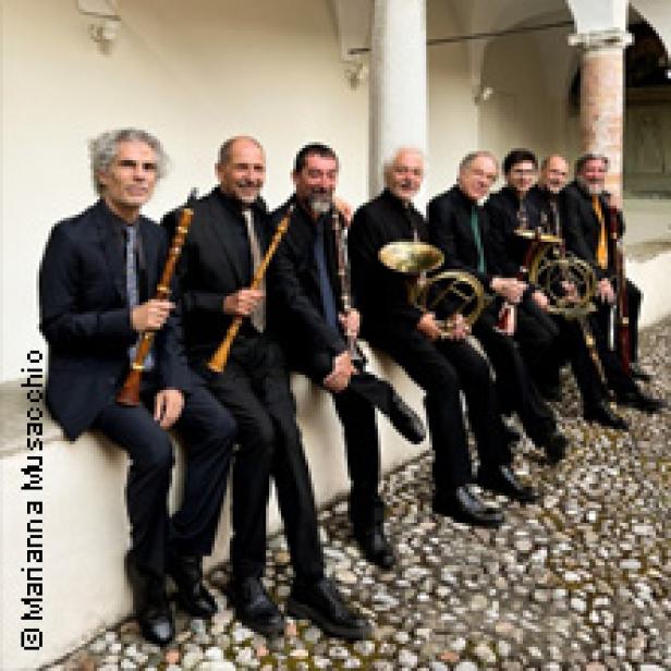 Eine Gruppe von acht Musikern sitzt mit ihren Instrumenten auf einer Mauer.