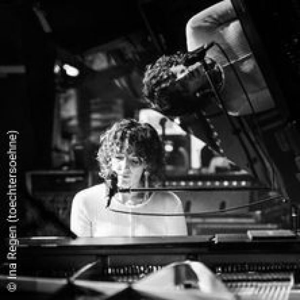 Eine Frau mit lockigem Haar spielt Klavier vor einem Mischpult.