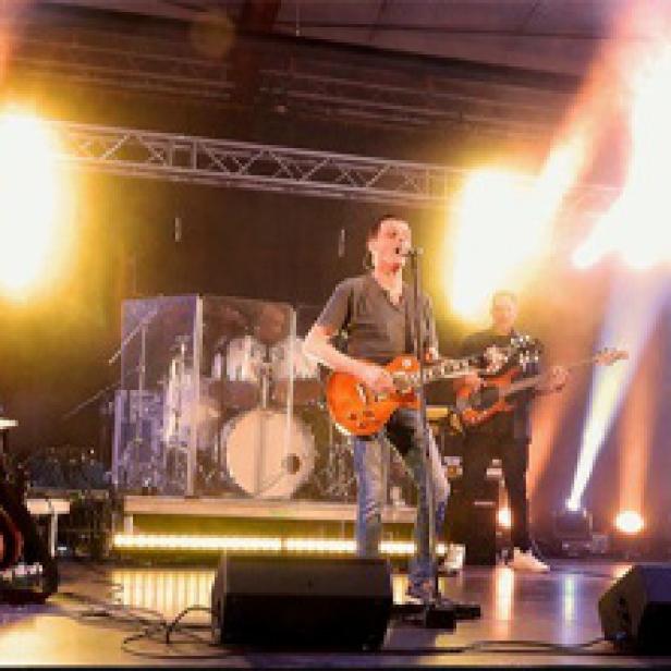 Ein Gitarrist steht auf einer Bühne während eines Konzerts.