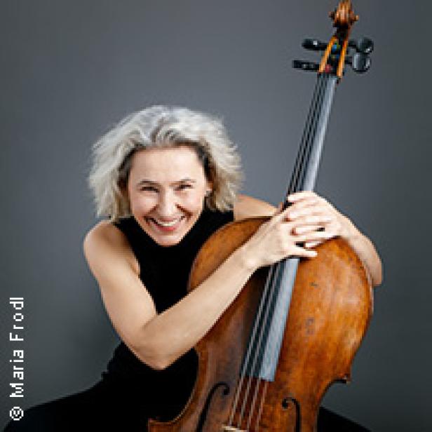 Eine lächelnde Frau mit grauem Haar umarmt ein Cello.