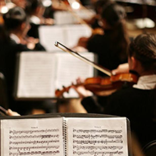 Ein Orchester spielt Musik, Notenblätter im Vordergrund.