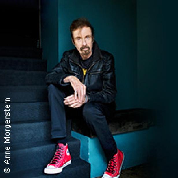 Ein Mann mit Bart und Lederjacke sitzt auf einer Treppe.
