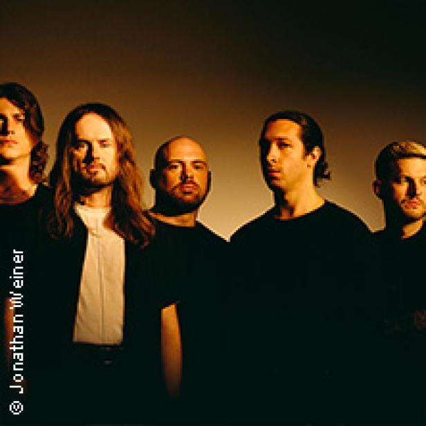 Fünf Männer stehen vor einem dunklen Hintergrund.