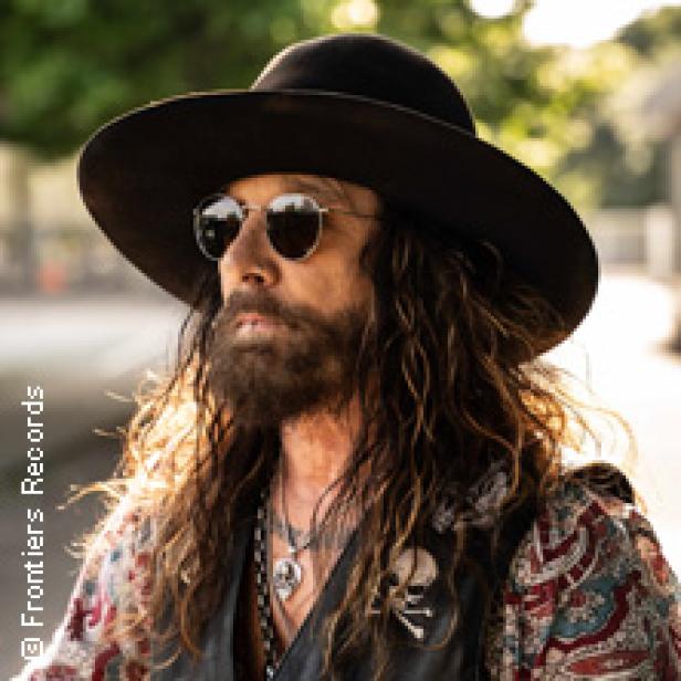 Ein Mann mit Bart, Hut und Sonnenbrille posiert für ein Foto.