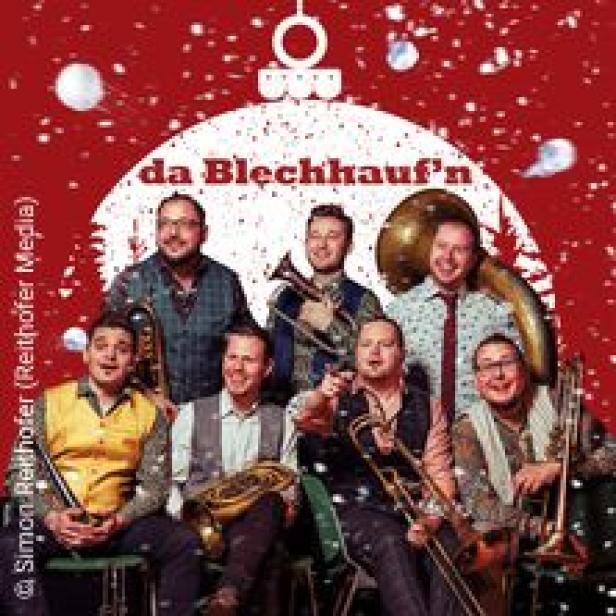Die Blaskapelle „da Blechhauf’n“ posiert vor einem weihnachtlichen Hintergrund.