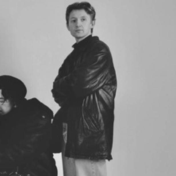 Ein Mann mit verschränkten Armen in einer schwarzen Jacke vor einem hellen Hintergrund.