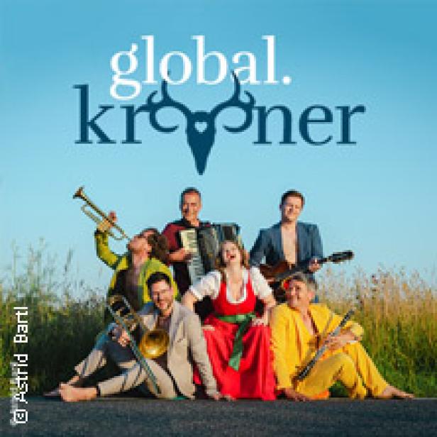 Die Band Global Kryner posiert mit ihren Instrumenten auf einer Landstraße.