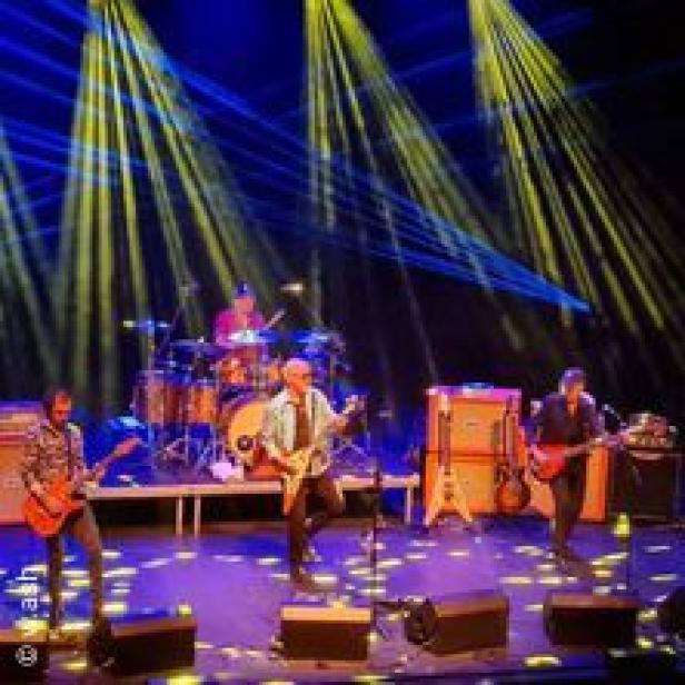 Eine Band spielt auf einer Bühne mit gelber und blauer Beleuchtung.