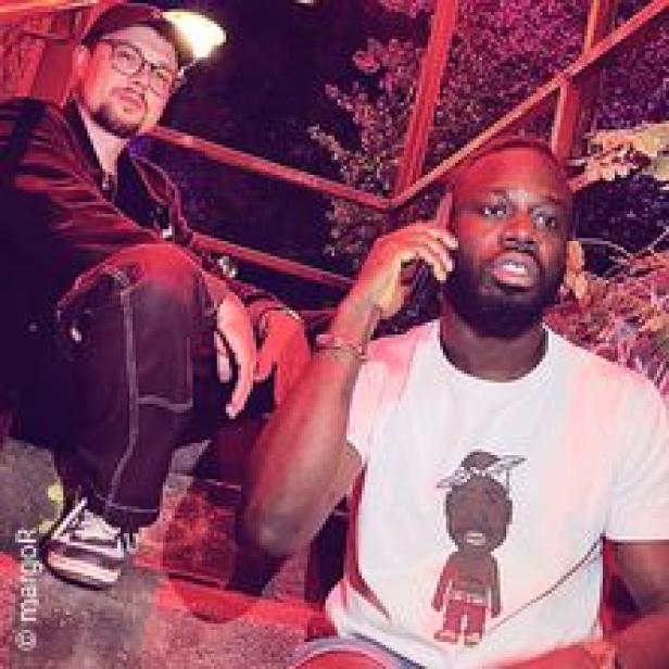 Zwei Männer posieren für ein Foto; einer telefoniert.