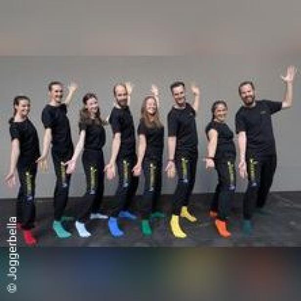 Eine Gruppe von acht Personen posiert in schwarzen Jogginghosen und T-Shirts mit bunten Socken.