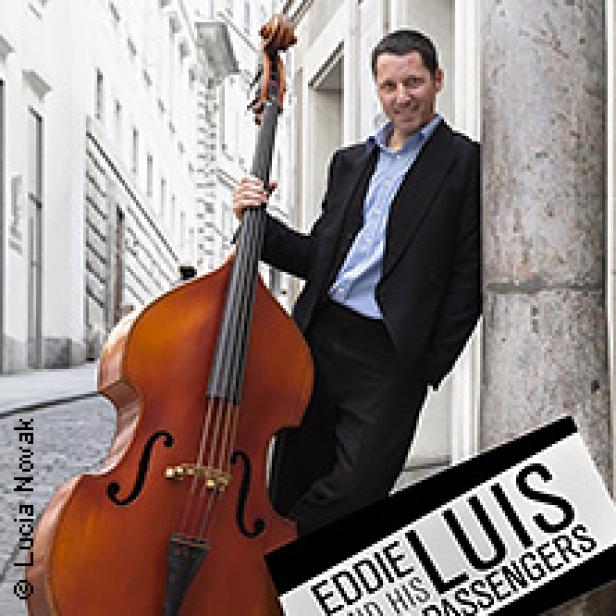 Ein Mann mit Kontrabass lehnt an einer Säule in einer Stadt.