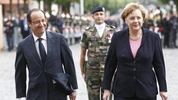 François Hollande und Angela Merkel schreiten an einem französischen Militärangehörigen vorbei.