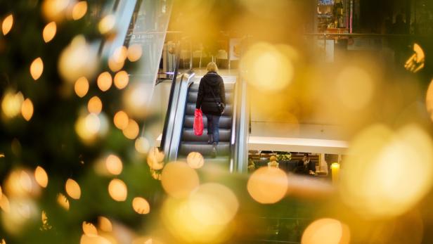 Eine Frau fährt in einem Einkaufszentrum mit einer Rolltreppe nach oben, im Vordergrund Weihnachtsdekoration.