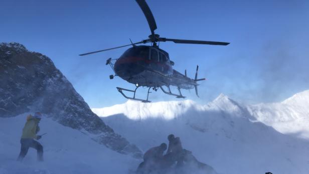 Ein Hubschrauber landet in einem verschneiten Berggebiet, während ein Mann mit Funkgerät zusieht.