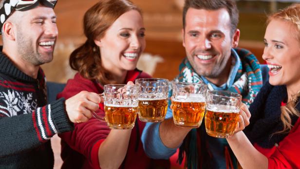 Eine Gruppe von vier Freunden stößt mit Bierkrügen an und lacht.