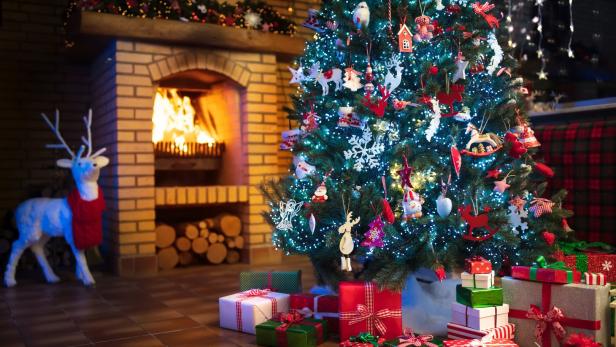 Ein festlich geschmückter Weihnachtsbaum steht vor einem Kamin mit brennendem Feuer.