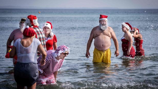 Eine Gruppe von Menschen in Weihnachtsmannkostümen watet im Meer.
