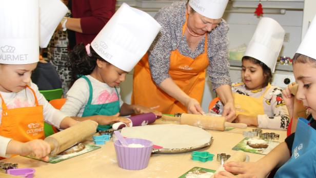 Kinder backen mit einer älteren Frau in einer Küche Kekse.