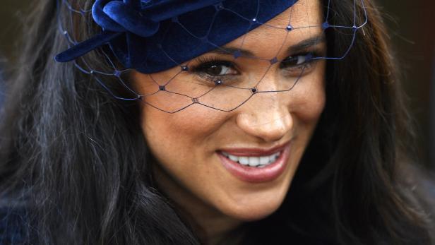 Meghan Markle mit einem blauen Hut und Schleier lächelt.