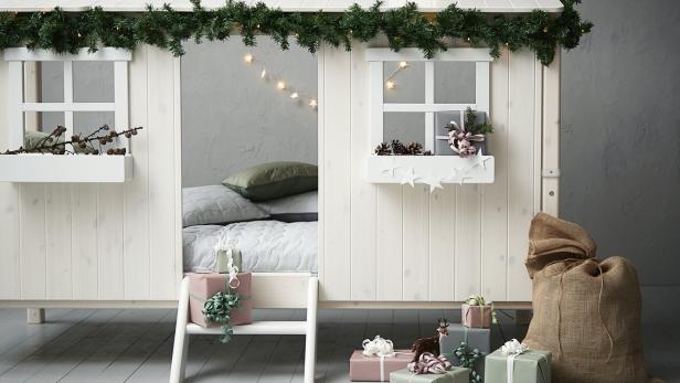 Ein weißes Kinderbett in Hausform ist weihnachtlich mit Geschenken und Tannengrün dekoriert.
