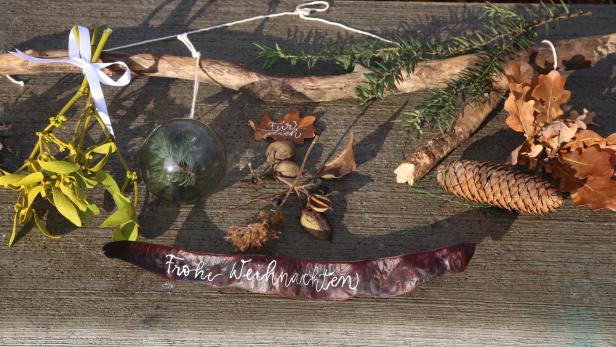 Ein weihnachtliches Arrangement mit Mistelzweig, Tannenzapfen und dem Schriftzug „Frohe Weihnachten“.