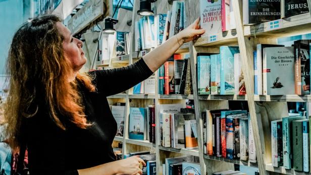 Eine Besucherin der Buch Wien Messe nimmt sich ein Buch aus einem Bücherregal
