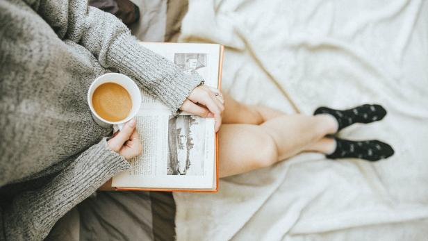 Ein Buch, eine Tasse Kaffee – auf dem Schoß einer Frau.