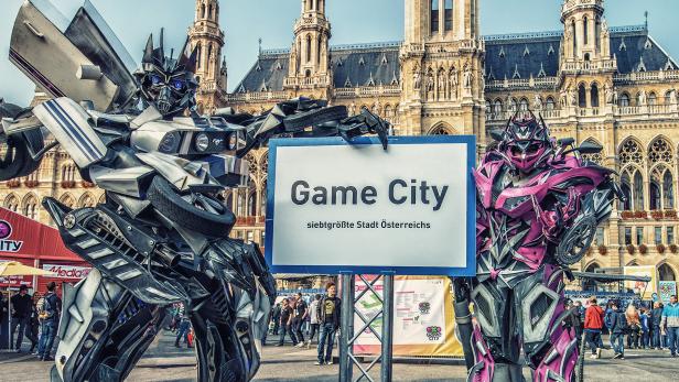 Große Mecha-Cosplayer posieren vor der Game City am Rathausplatz mit Schild "Game City - siebtgrößte Stadt Österreichs"
