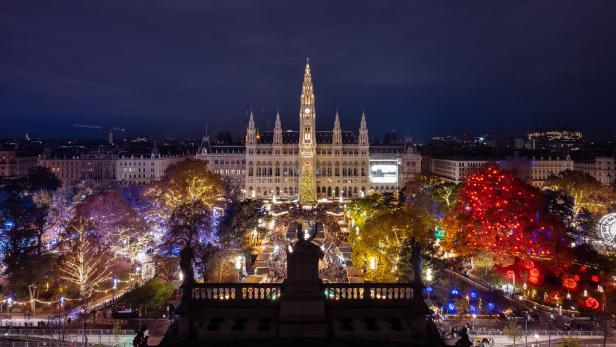 Blick auf das Rathaus vom Burgtheater aus gesehen. Mittig der Markt, links und rechts die beleuchtete Weihnachtswelt im Park.