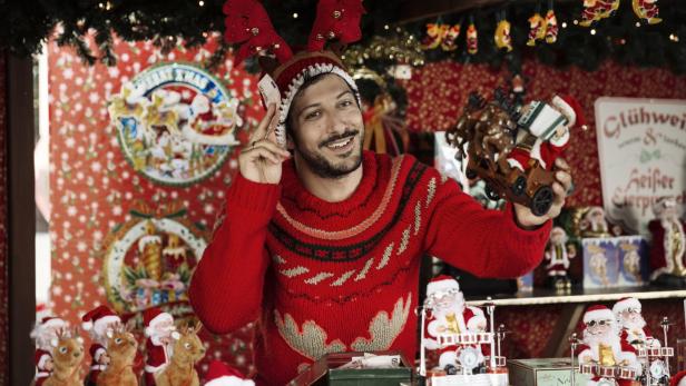 Ein Mann mit Rentiergeweih verkauft Weihnachtsdekorationen auf einem Weihnachtsmarkt.