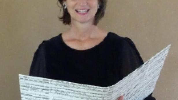 Eine Frau mittleren Alters hält ein aufgeschlagenes Notenbuch in ihren Händen.