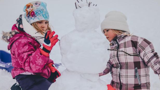 Zwei Kinder bauen einen Schneemann.