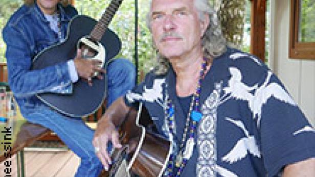 Zwei Musiker, der eine mit Hut und Sonnenbrille, posieren mit ihren Gitarren.