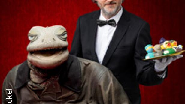 Ein Mann im Anzug präsentiert eine Echsenpuppe mit Zigarre und ein Tablett mit Süßigkeiten.