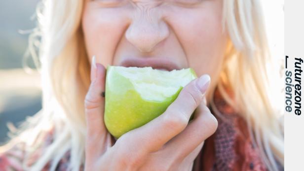 Eine blonde Frau beißt in einen grünen Apfel und verzieht dabei das Gesicht