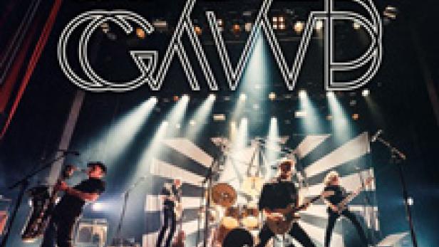 Die Band Spidergawd spielt live auf einer Bühne mit Scheinwerfern und einem schwarz-weiß gestreiften Hintergrund.