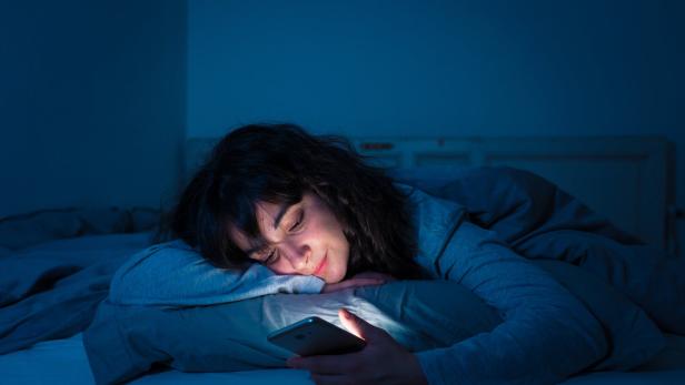 Frau in blauem Licht im Bett mit Handy 