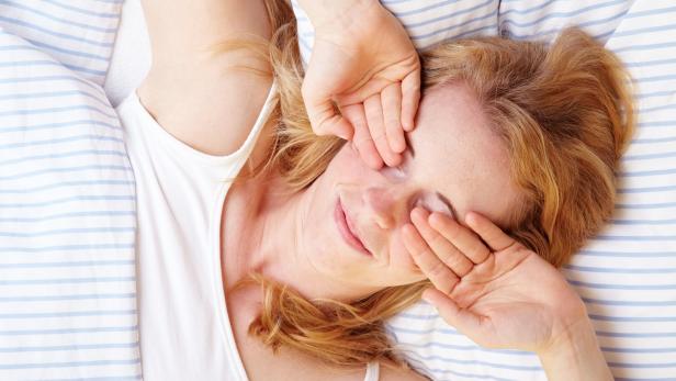 Frau um Bett reibt sich die Augen