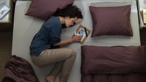 Trauernde Frau liegt mit Foto des verstorbenen am Bett