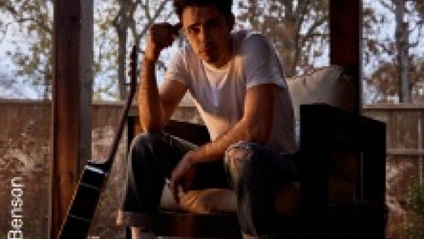 Ein Mann sitzt mit einer Gitarre auf einer Veranda.